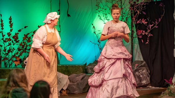 Zwei Frauen in farbenfrohen Kleidern stehen auf der Bühne der Oregon Episcopal School vor einem blumigen Hintergrund.