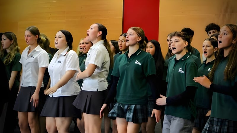 Eine Gruppe von Schülern des Orewa College singt gemeinsam auf der Bühne vor einem roten Vorhang.