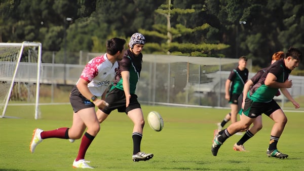 Eine Gruppe Schüler spielt Sport auf dem grünen Sportplatz des Orewa College mit einem Tor im Hintergrund.