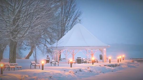 Ein schneebedeckter Pavillon mit beleuchteten Laternen und Stühlen auf dem Campus der Orillia Secondary School in einer Winterlandschaft.