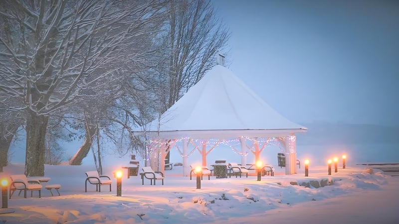 Ein schneebedeckter Pavillon mit beleuchteten Laternen und Stühlen auf dem Campus der Orillia Secondary School in einer Winterlandschaft.