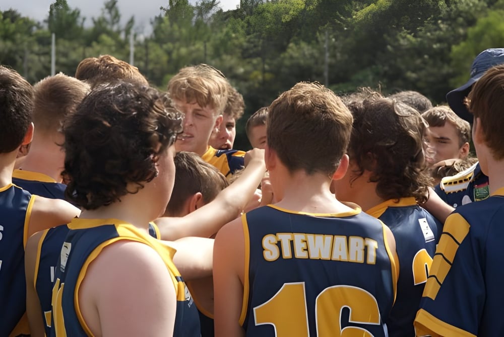 Eine Gruppe junger Sportler steht im Freien auf einer Wiese auf dem Campus der Ormeau Woods State High School mit Blick auf die Bäume.