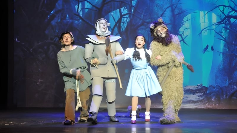 Schüler der Oromocto High School führen in verschiedenen Kostümen auf einer Bühne vor einem dunklen Waldhintergrund auf.