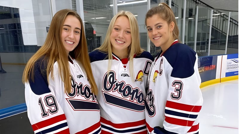 Drei Schülerinnen der Orono High School stehen in Hockey-Jerseys auf der Eisbahn in der Sporthalle.