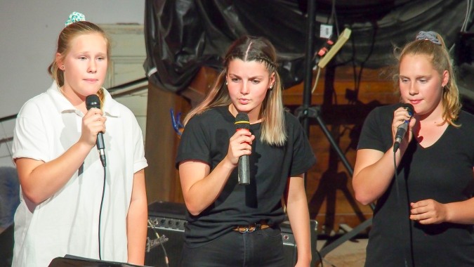 Drei Schülerinnen der Orroroo Area School stehen mit Mikrofonen auf einer Bühne und führen eine Gesangsperformance auf.