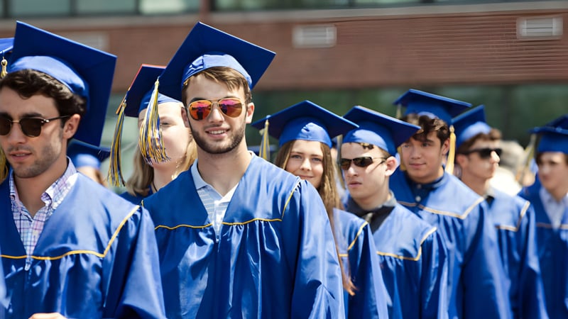 Eine Gruppe von Absolventinnen und Absolventen der Osgoode Township High School steht vor einem Backsteingebäude in blauen Talaren und Mützen.