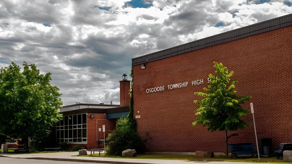 Das Backsteingebäude der Osgoode Township High School ist von Bäumen umgeben unter bewölktem Himmel.