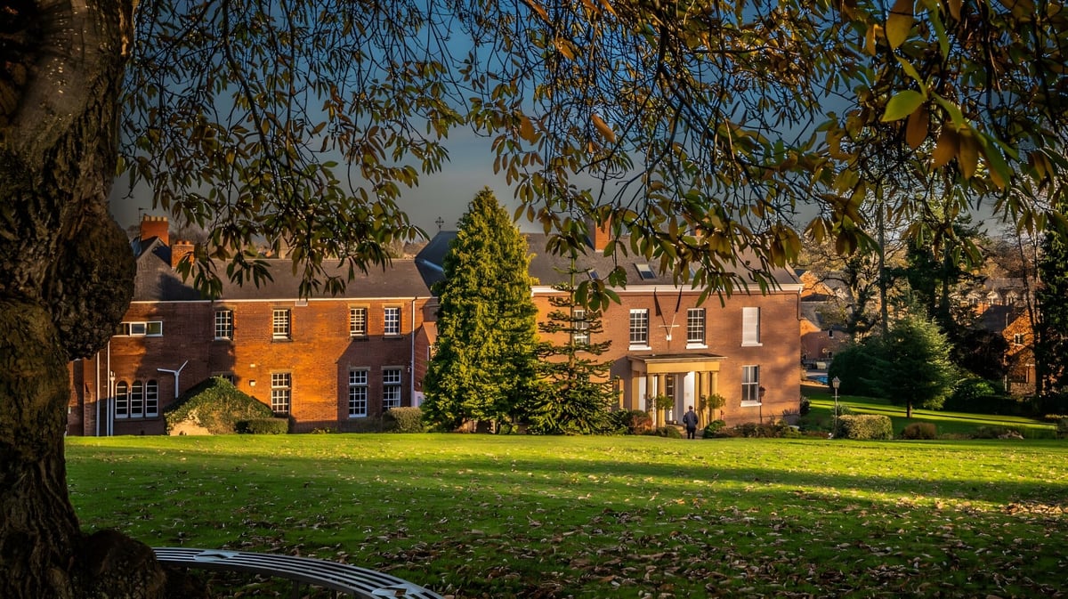 Das Backsteingebäude der Oswestry School ist umgeben von grüner Landschaft unter klarem blauem Himmel.