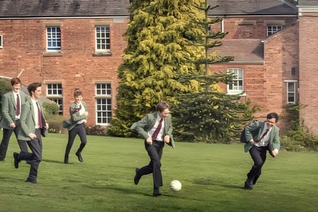 Eine Gruppe von Menschen in Freizeitkleidung spaziert über eine Grasfläche vor einem Backsteingebäude auf dem Gelände der Oswestry School.
