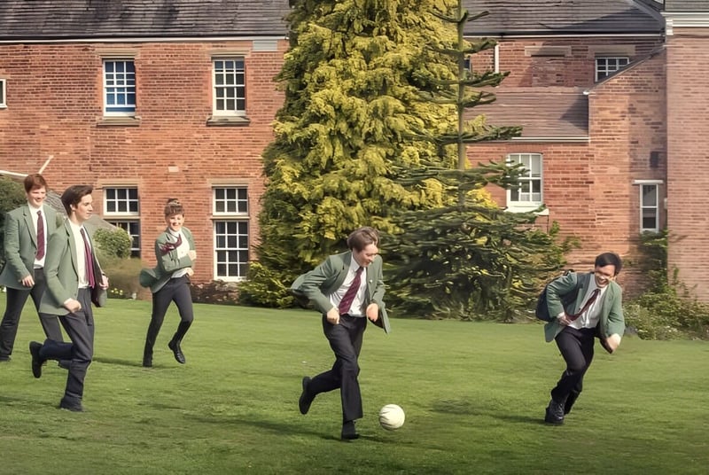 Eine Gruppe von Menschen in Freizeitkleidung spaziert über eine Grasfläche vor einem Backsteingebäude auf dem Gelände der Oswestry School.