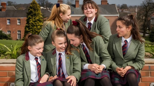 Schülerinnen in grünen Blazern und roten Röcken auf dem Campus der Oswestry School stehen zusammen und unterhalten sich.