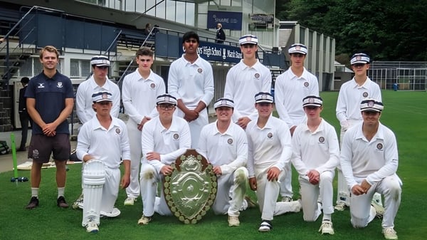 Eine Gruppe von Schülern der Otago Boys' High School posiert auf einem Cricketfeld mit Stadion im Hintergrund.