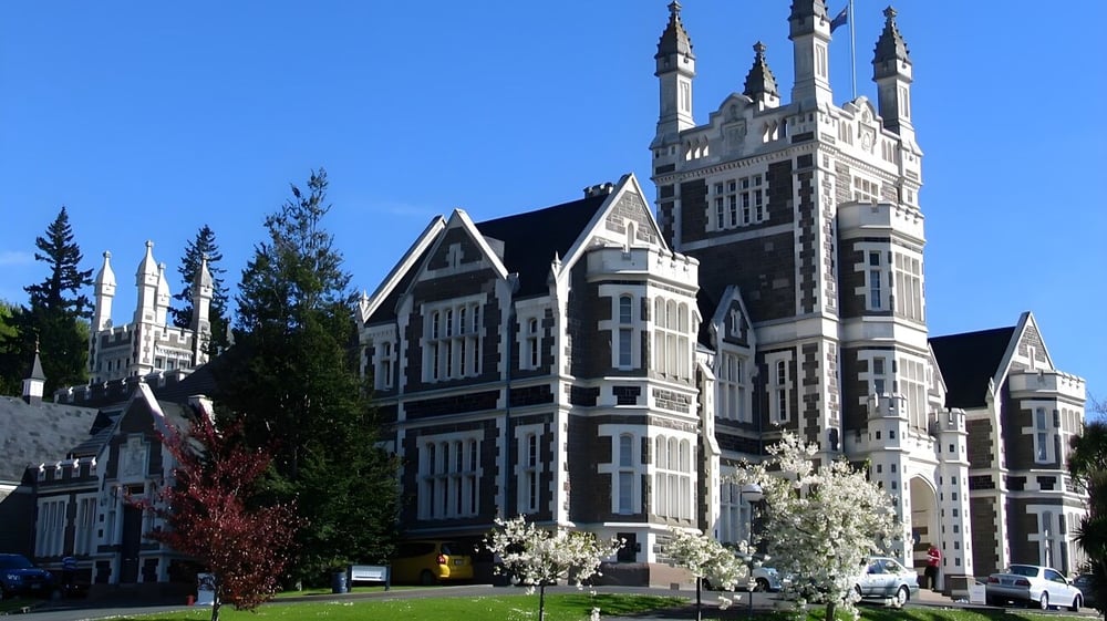 Das gotische Hauptgebäude der Otago Boys' High School steht umgeben von Bäumen und einem grünen Rasen.