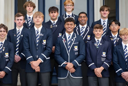 Eine Gruppe Schüler steht vor dem Gebäude der Otago Boys' High School mit großen Fenstern.