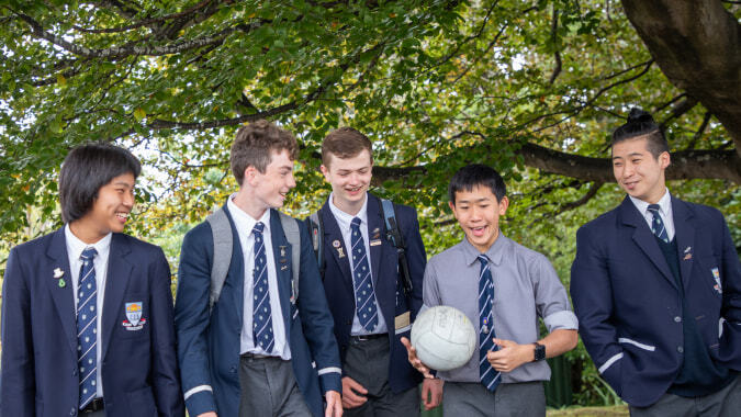 Eine Gruppe von Schülern der Otago Boys' High School steht im grünen Außenbereich zusammen.