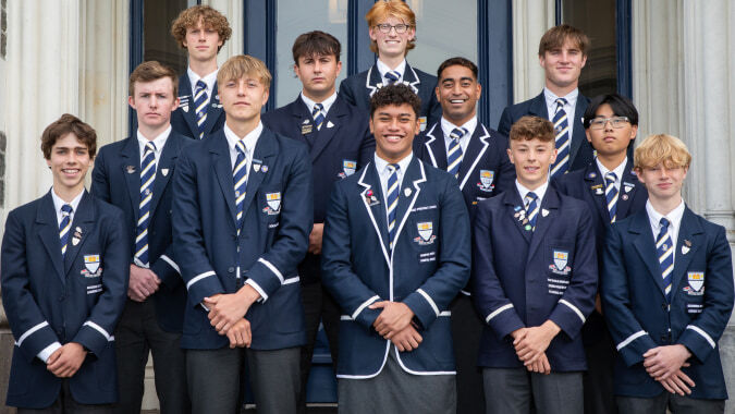 Eine Gruppe Schüler der Otago Boys' High School steht vor einem verzierten Gebäude mit Rundbogenfenstern.