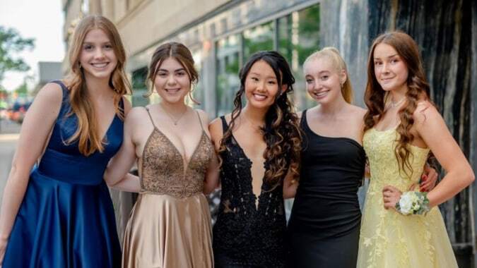 Fünf Schülerinnen der Otago Girls High School stehen in formeller Kleidung vor einem Gebäude mit Glasfassade bei einer Veranstaltung.