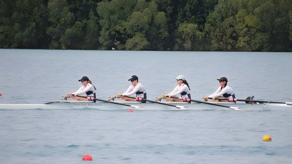 Vier Schülerinnen der Otago Girls High School rudern gemeinsam auf einem ruhigen See in einer bewaldeten Landschaft.