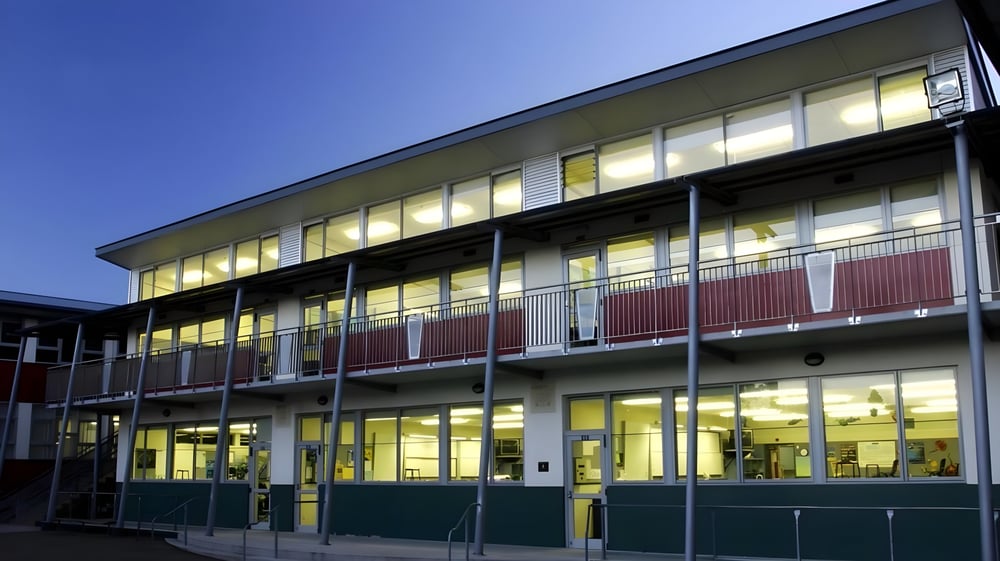 Das mehrstöckige Gebäude des Otumoetai College mit großen Fenstern und grünem Sockel vor blauem Himmel.