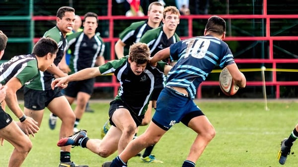 Schüler des Otumoetai College spielen ein intensives Rugby-Match auf einem mit Zaun umgebenen Spielfeld.