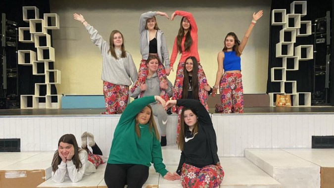 Eine Gruppe junger Schülerinnen steht auf der Bühne des Our Lady Catholic College vor einem geometrischen Bühnenbild.