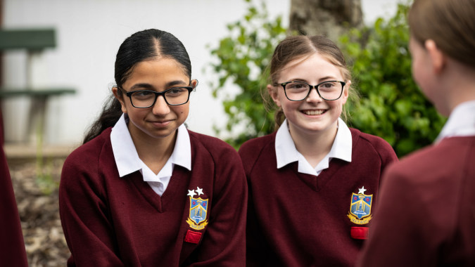 Zwei Schülerinnen des Our Lady Catholic College stehen gemeinsam in einem Garten mit grünem Hintergrund.