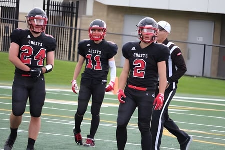 Eine Gruppe junger Fußballspieler steht auf dem Spielfeld der Our Lady of the Rockies High School vor einem Schulgebäude.