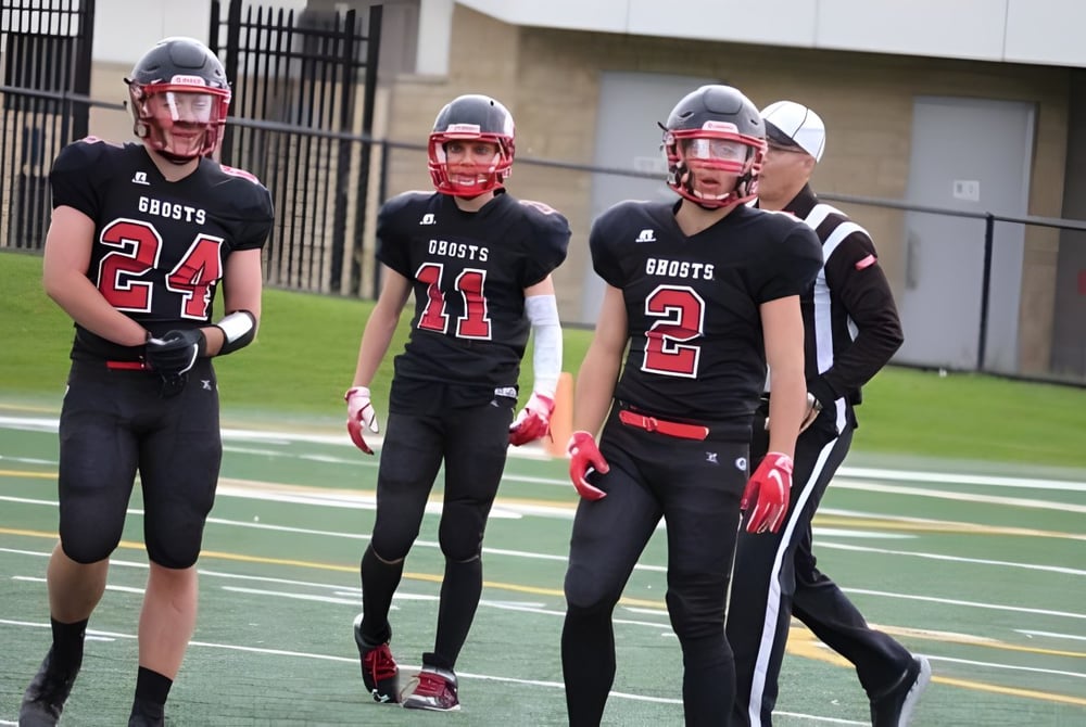 Eine Gruppe junger Fußballspieler steht auf dem Spielfeld der Our Lady of the Rockies High School vor einem Schulgebäude.