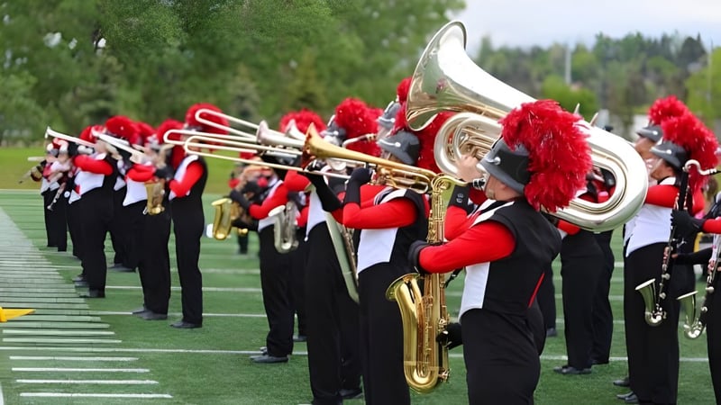 Die Marching Band der Our Lady of the Rockies High School tritt auf einem Grasfeld mit Wald im Hintergrund auf.