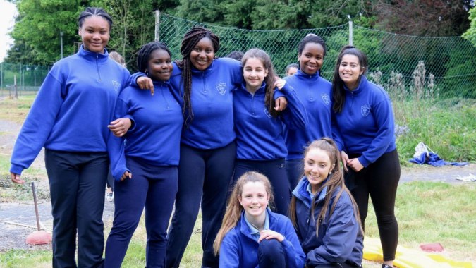 Schülerinnen der Our Lady´s Bower Secondary School stehen draußen in blauen Uniformen vor grüner Umgebung.
