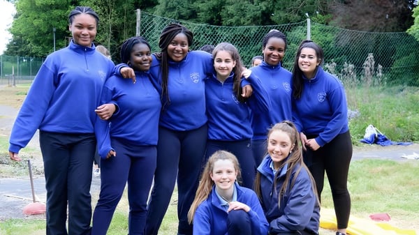 Eine Gruppe Schülerinnen der Our Lady's Bower Secondary School steht draußen auf einer Wiese mit Bäumen und Zaun im Hintergrund.
