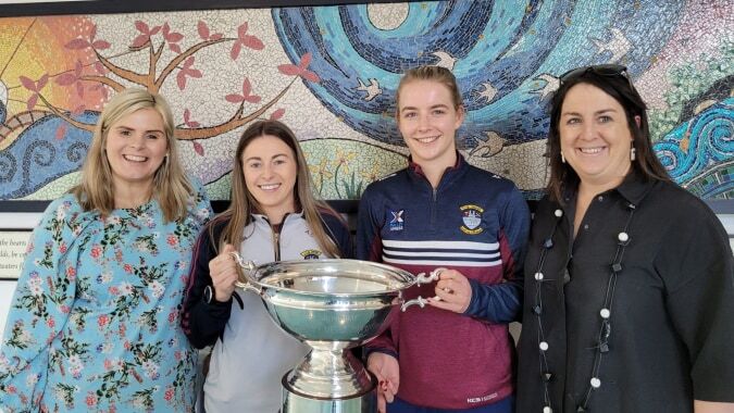 Vier Schülerinnen der Our Lady´s Bower Secondary School halten lächelnd eine Trophäe vor einem bunten Wandbild mit Natur- und Abstraktmotiven.