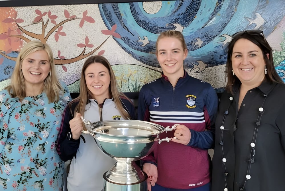 Vier Schülerinnen der Our Lady´s Bower Secondary School halten gemeinsam einen Pokal vor einer farbenfrohen Wandmalerei.