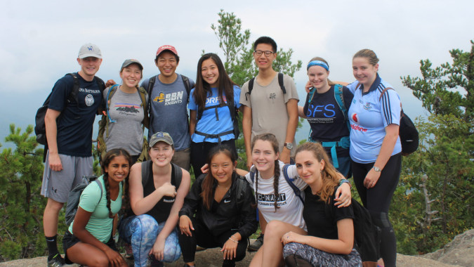 Eine Gruppe Schülerinnen und Schüler steht im Freien vor Kiefern auf dem Gelände der Our Lady’s Secondary School.