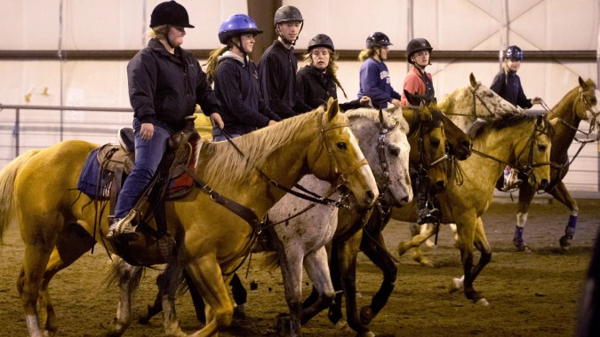 Schüler der Our Lady’s Secondary School beim Reiten in einer Reithalle mit dunkler Kleidung und Helmen.