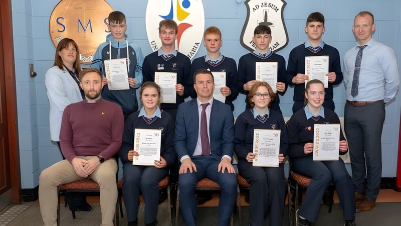 Eine Gruppe von Schülerinnen, Schülern und Lehrkräften von Our Lady’s Secondary School posiert vor einem Schulbanner mit Zertifikaten.
