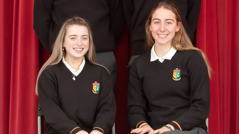 Zwei Schülerinnen in schwarzen Schuluniformen stehen vor einem roten Vorhang auf dem Campus der Our Lady’s Secondary School.