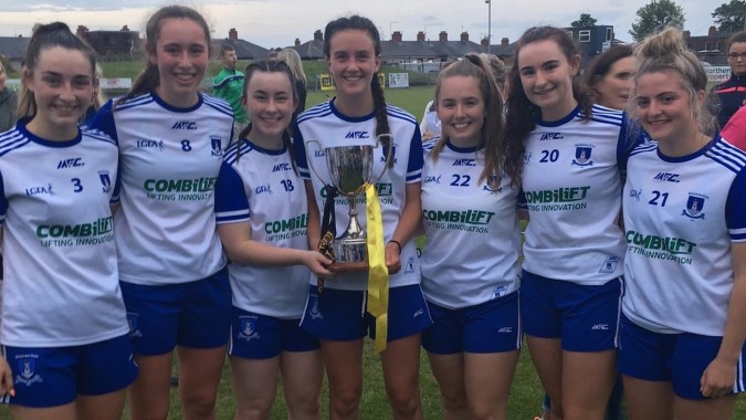 Eine Gruppe von Fußballspielerinnen der Our Lady’s Secondary School hält einen Pokal auf dem Sportfeld vor Schulgebäuden.
