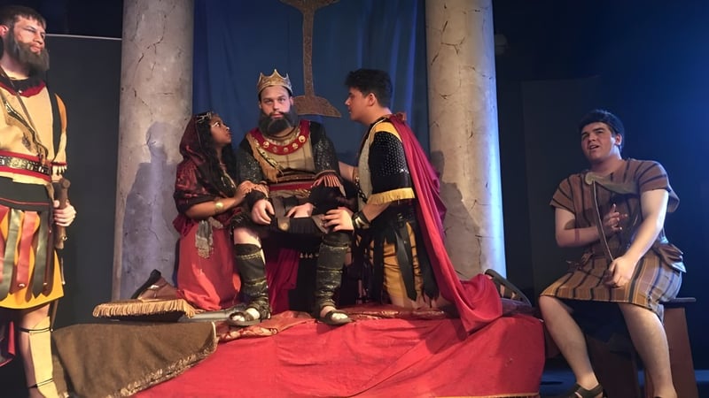 Schüler der Our Savior New American School führen eine theatrale Szene mit kostümierten Darstellern auf einer Bühne auf.