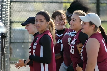 Eine Gruppe junger Athletinnen steht zusammen auf dem Sportfeld der Our Savior New American School nahe einem Maschendrahtzaun.