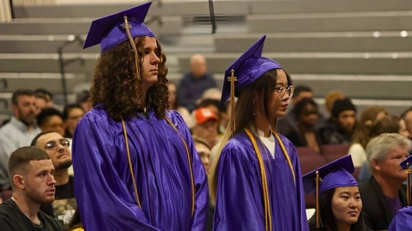 Eine Gruppe von Absolventinnen und Absolventen in violetten Talaren steht in der Aula der Overland Christian Schools.