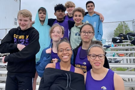 Eine Gruppe Schülerinnen und Schüler der Overland Christian Schools steht lächelnd im Freien vor einem Zaun und Tribünen.