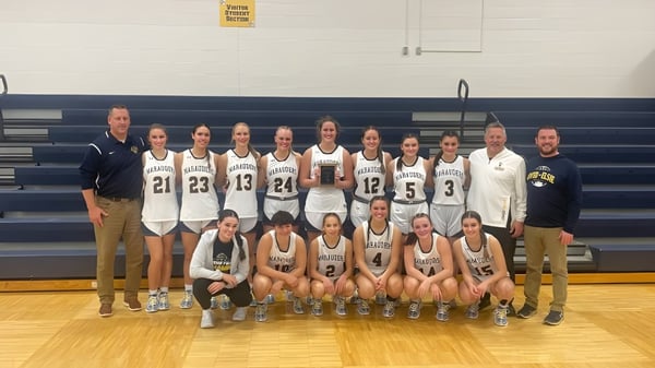 Eine Gruppe weiblicher Basketballspielerinnen und Trainerinnen der Ovid-Elsie High School posiert gemeinsam auf dem Basketballfeld.