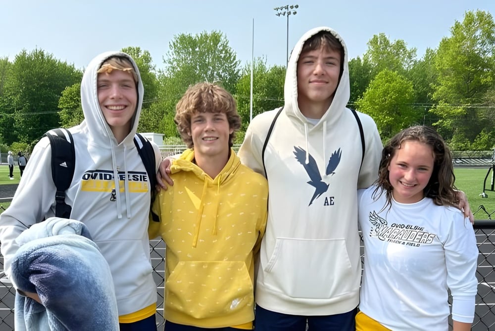 Vier Schülerinnen und Schüler der Ovid-Elsie High School stehen gemeinsam auf einem Sportfeld im Freien.