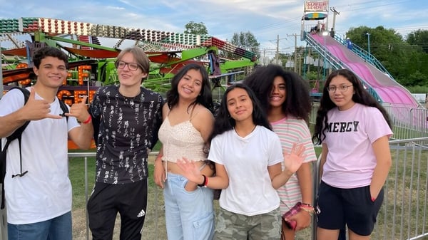 Schüler der Oxford Academy stehen vor einem bunten Freizeitpark mit Fahrgeschäften im Hintergrund.