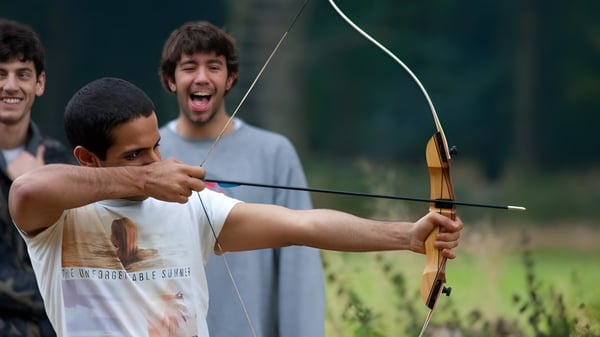Schüler des Oxford International College Brighton beim Bogenschießen auf einer Wiese im Freien.