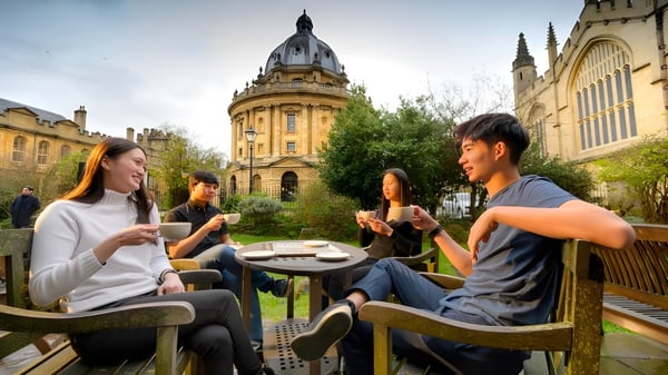 Eine Gruppe von Schülerinnen und Schülern unterhält sich und genießt Getränke auf dem Außengelände des Oxford International College vor historischem Gebäude.
