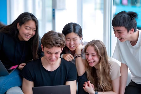 Schüler des Oxford International College arbeiten gemeinsam an einem Tablet in einem Raum mit bunten Wänden und Fenstern.