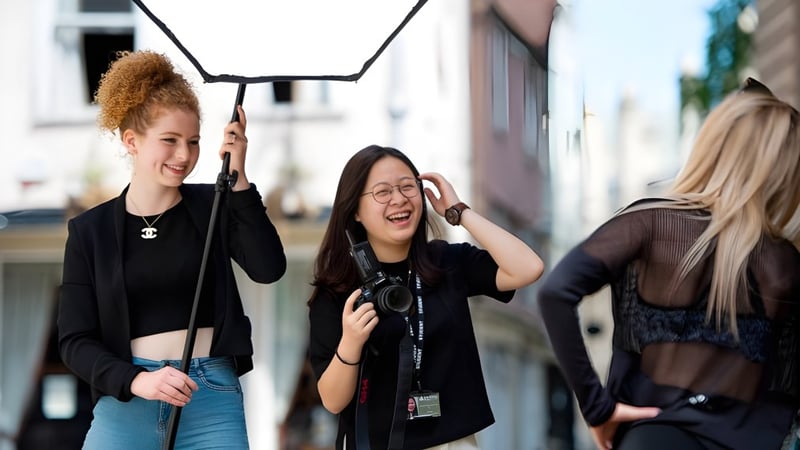 Eine Gruppe Schülerinnen interagiert lachend im Außenbereich des Oxford Sixth Form College vor Gebäuden.