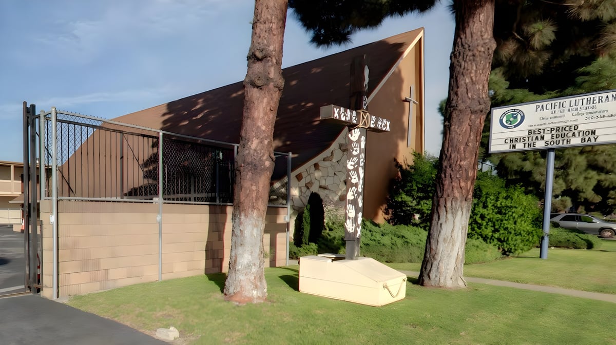 Das moderne Gebäude der Pacific Lutheran High School mit dreieckigem Dach steht in einem grasbewachsenen Bereich mit hohen Palmen.